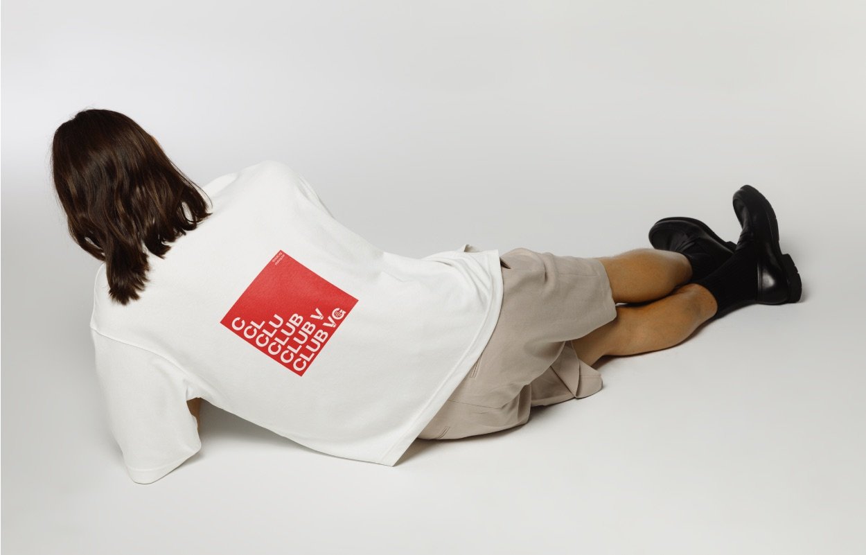T-shirt blanc floqué du visuel typographique rouge Club VG, porté par une personne allongée au sol.
