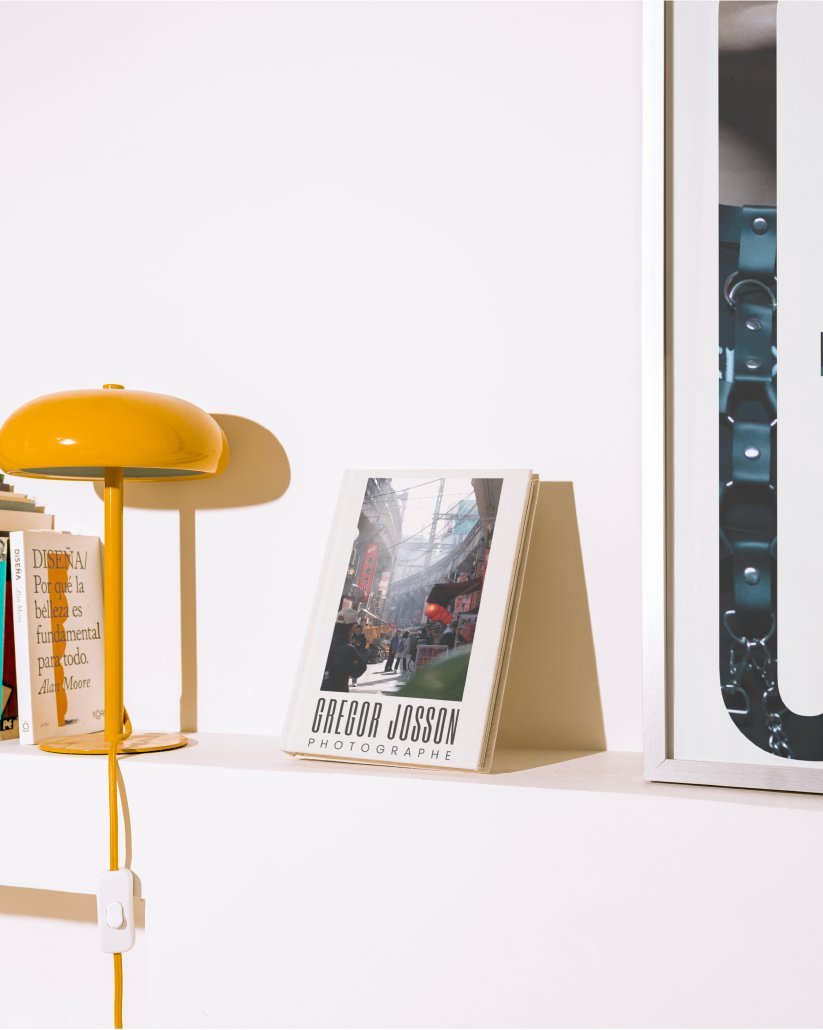 Livre de photographies Gregor Josson posé sur une étagère, à côté d’une lampe jaune.